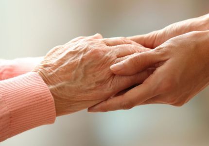 Seniorin hält Hand mit pflegendem Angehörigen